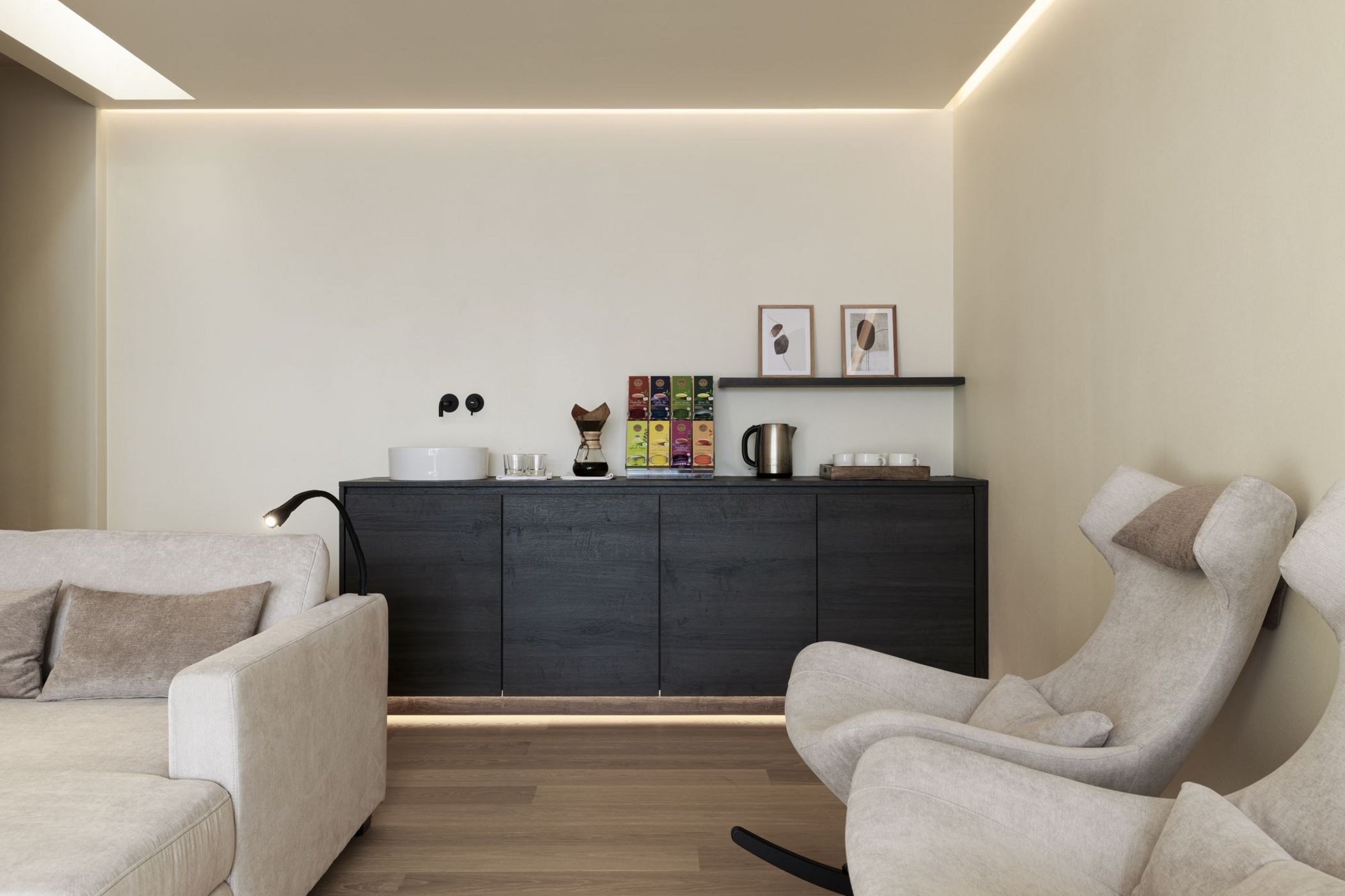 Soggiorno moderno con divano chiaro, poltrone e mobile nero con caffettiera e accessori da tè.