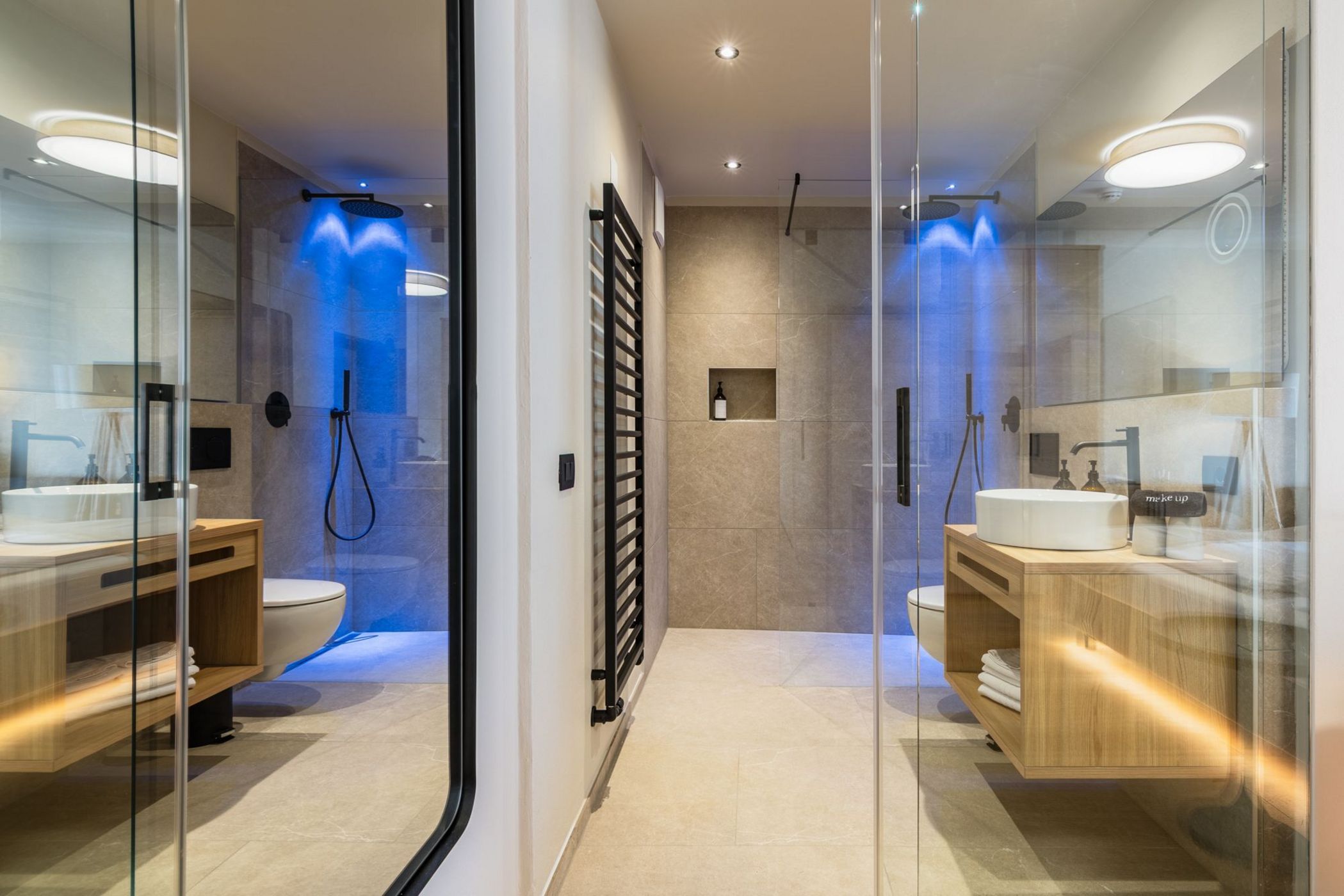 Bagno moderno con doccia a pioggia illuminata di blu e mobili in legno chiaro.