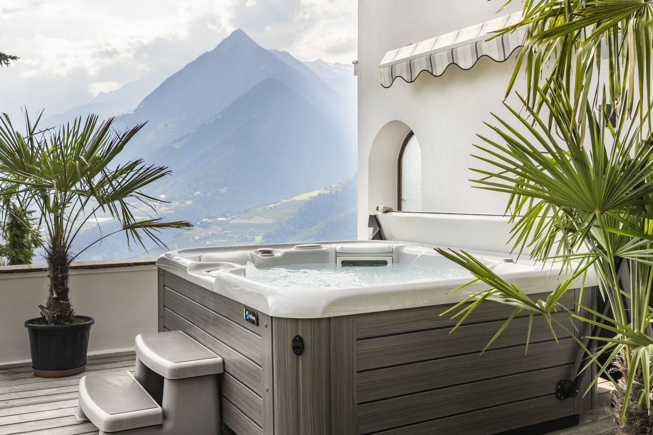 Vasca idromassaggio su terrazza con piante e vista sulle montagne nebbiose.