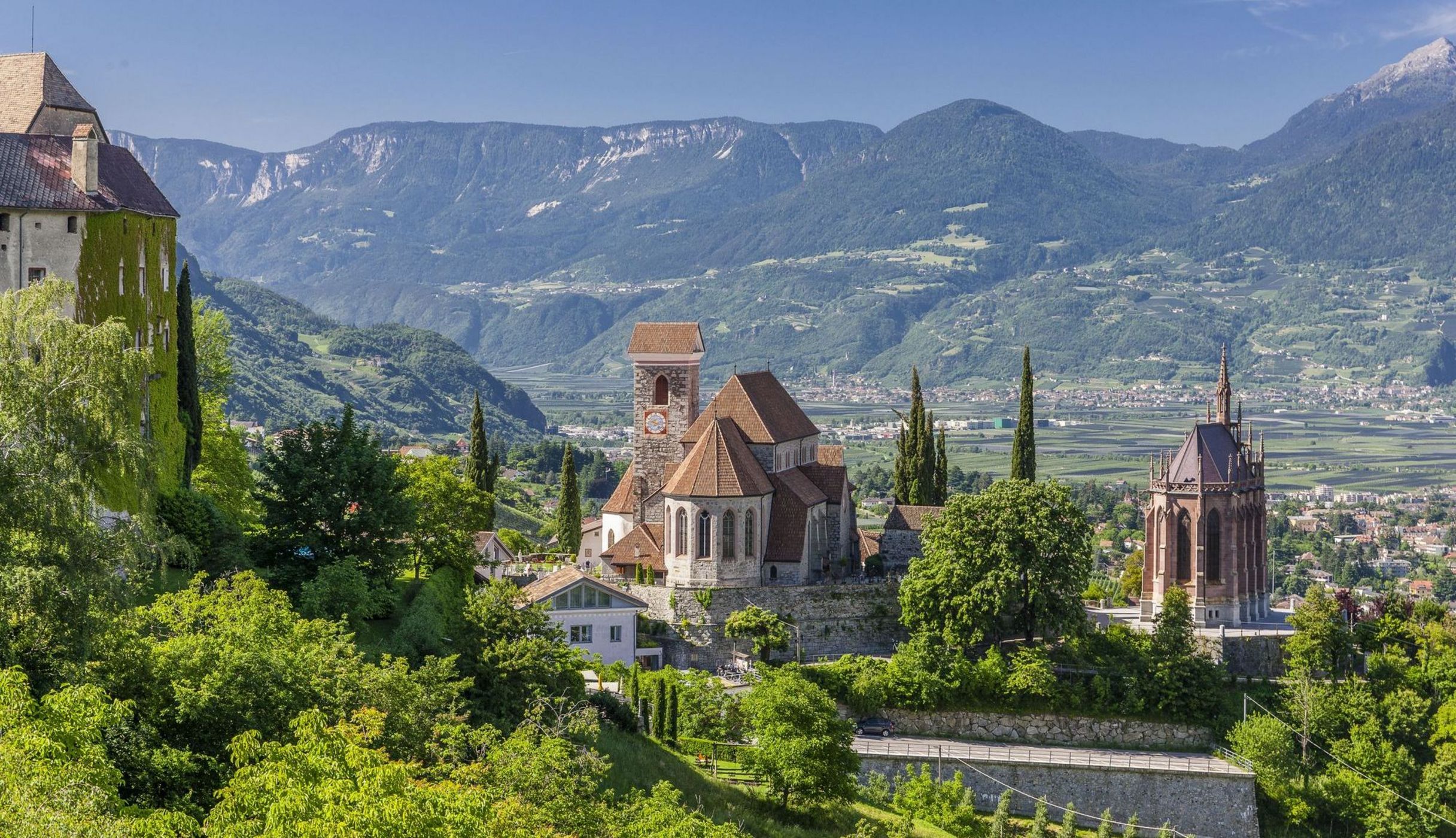 Panorama di un villaggio con chiese storiche e montagne sullo sfondo in una giornata soleggiata.