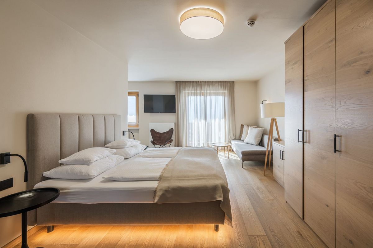 helles, modernes Schlafzimmer mit Doppelbett, Sofa, Holzschrank und Fernseher