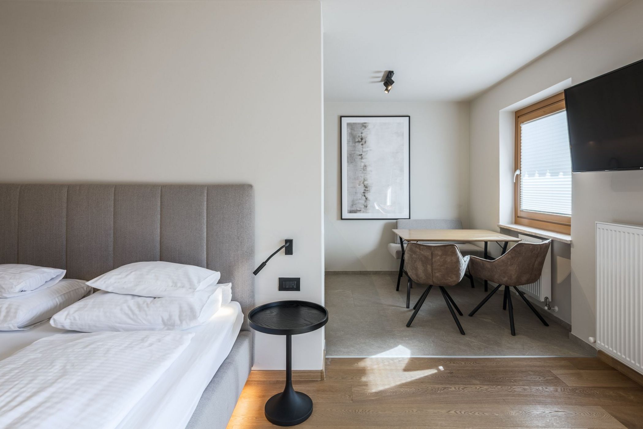 Camera moderna con letto matrimoniale, tavolo da pranzo con sedie, finestra e televisore a parete.